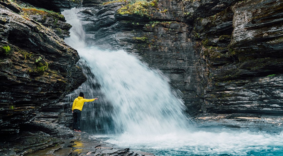 Kvinna som sträcker armarna mot ett vattenfall