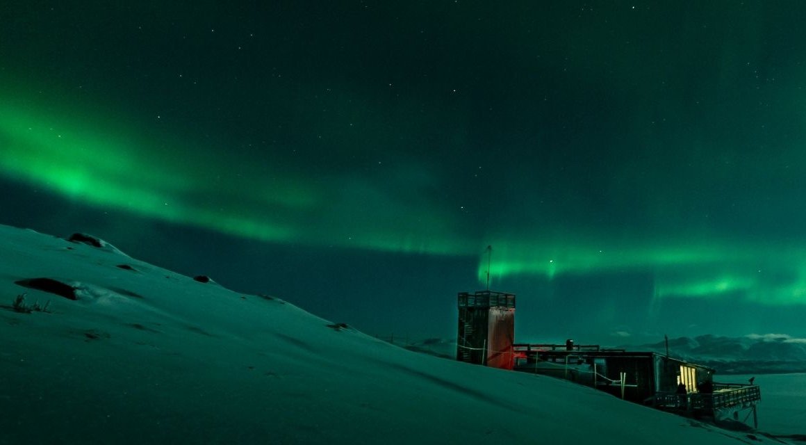 ett grönt norrsken som sverper fram över natthimlen ovan Abisko